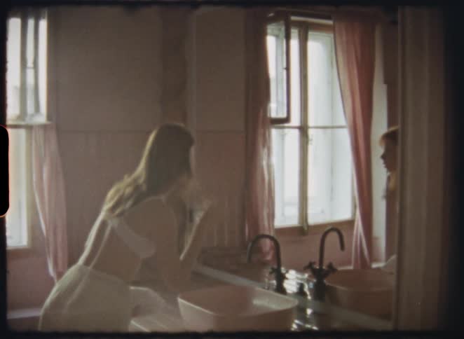An intimate 8mm film captures a young woman in her underwear performing her morning routine in a softly lit, vintage bathroom