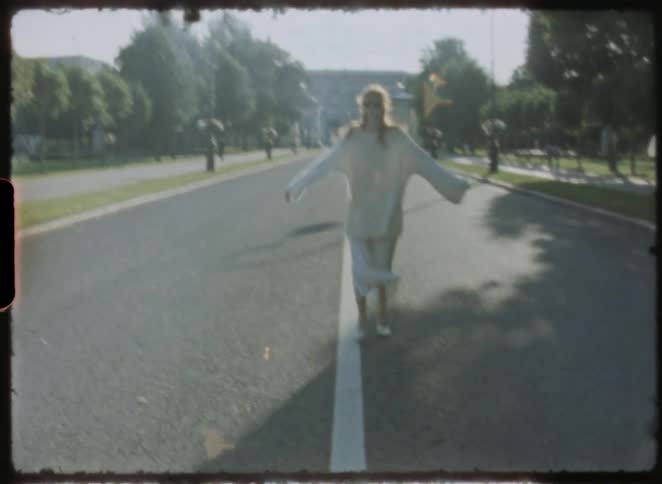 Dreamy vintage footage of a carefree woman in white balancing on the white line of an empty, sunlit city road