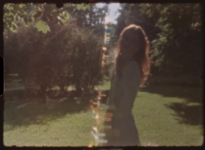 Artistic vintage footage of a young woman playfully posing in a sun-drenched park, with dreamy light leaks and unique shaped lens flares creating a nostalgic mood