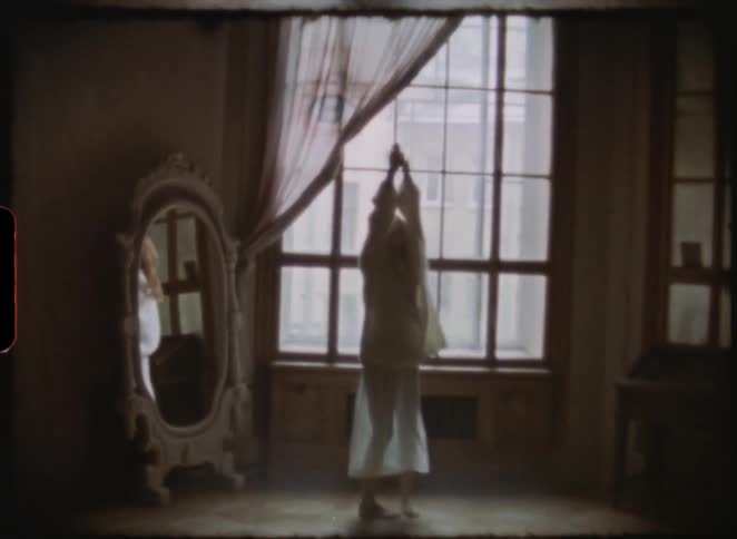 Dreamlike vintage 8mm footage captures a woman dancing gracefully by a window in a dimly lit, classic room