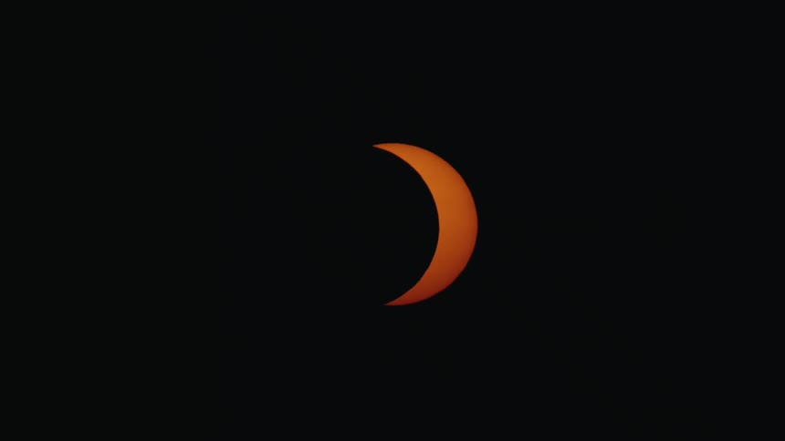 A time-lapse of an orange crescent sun moving across a black sky during a partial solar eclipse