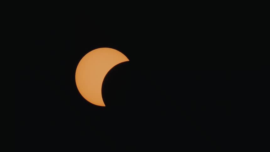 A time-lapse shows a partial solar eclipse as the moon's shadow moves across the orange sun