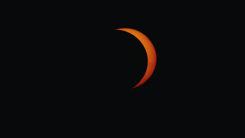 Close-up of the sun as a fiery orange crescent during a partial solar eclipse against the darkness of space