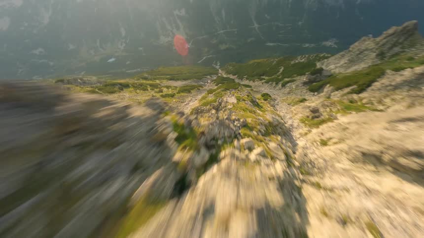 A thrilling FPV drone dive down a steep and rocky mountain ridge during a hazy sunrise