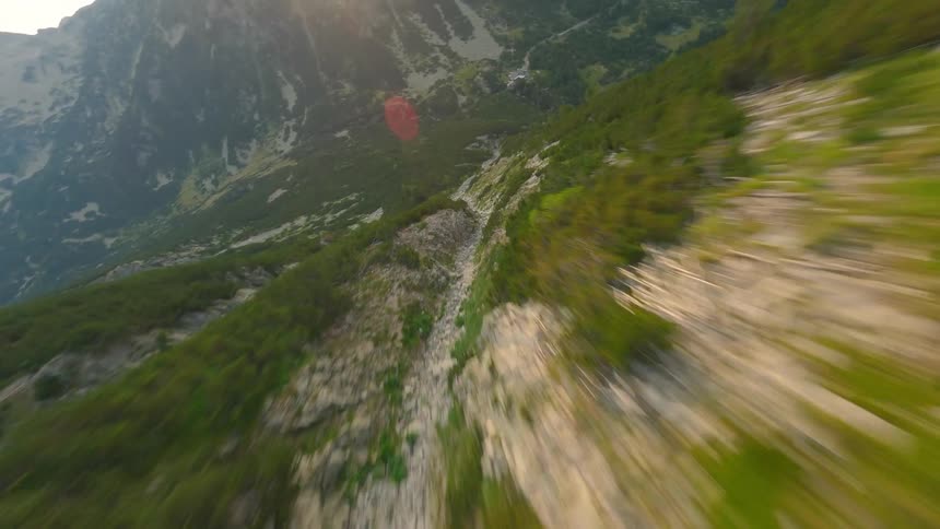 A high-speed FPV drone dives down a lush green mountain slope, revealing the rocky valley below