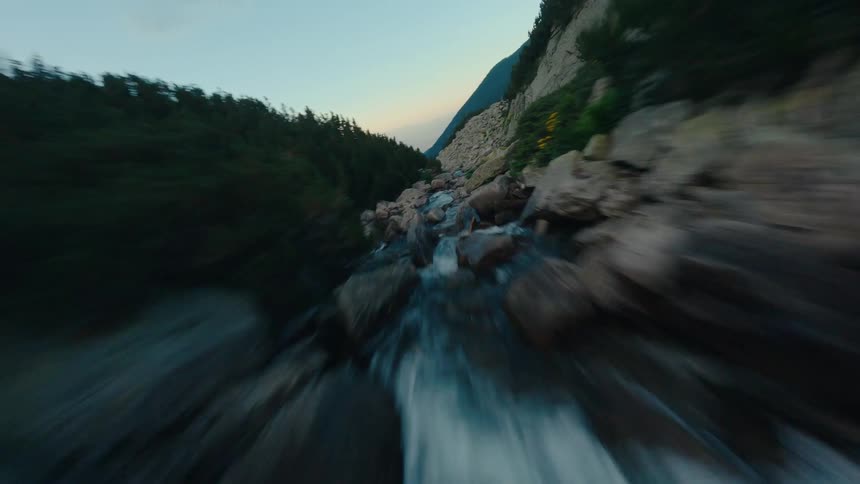 An immersive FPV drone races up a rocky mountain river, navigating through a breathtaking valley at twilight