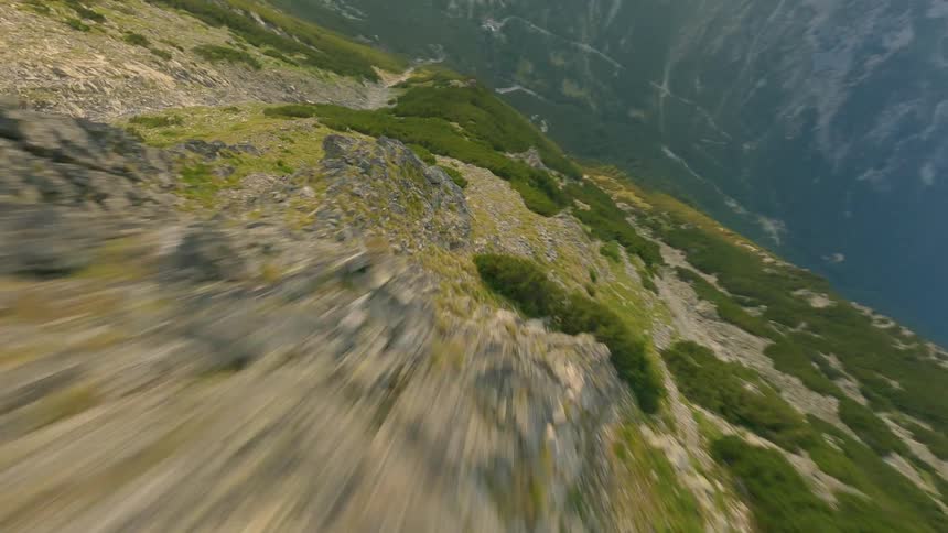 A thrilling first-person-view drone flight speeds along a green mountain ridge before diving steeply into the expansive valley below