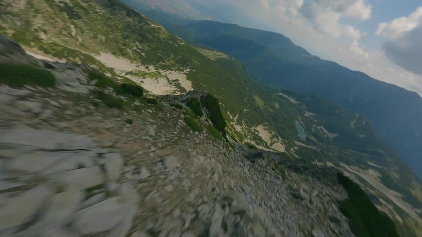 A breathtaking FPV drone flight soars over a rugged mountain ridge, then dives steeply down the rocky cliffside