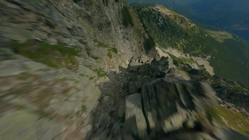 A thrilling FPV drone dive down a steep and rugged mountain cliff face reveals the vast landscape below