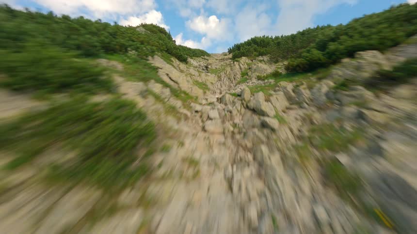 Fast-paced FPV drone footage pulling back down a steep, rocky slope covered in scree and patches of alpine greenery