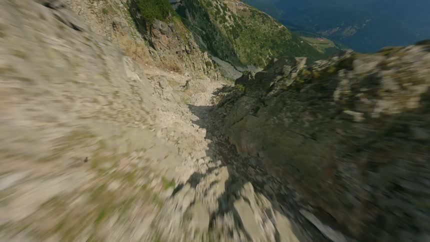 A thrilling first-person view drone flight dives down a steep and rocky mountain ravine at exhilarating speed