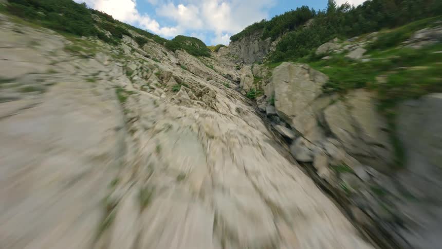 A fast-paced FPV drone navigates a steep, rocky mountain gorge under a blue sky