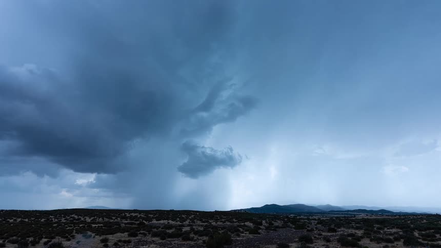 An intense lightning storm rages with dark, churning clouds and heavy rain over a vast, arid landscape