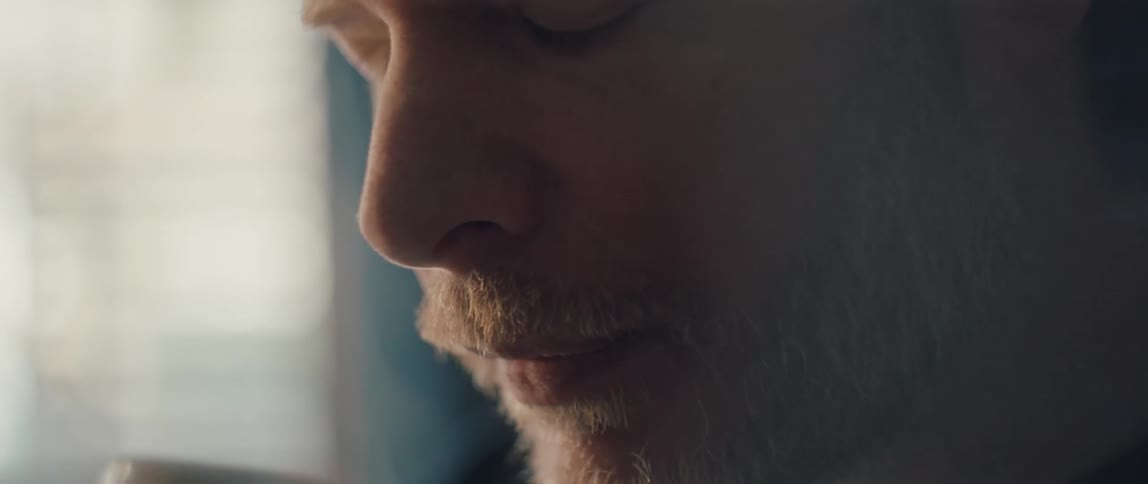 A thoughtful man with a graying beard slowly sips a hot beverage from a white mug in a quiet moment of contemplation