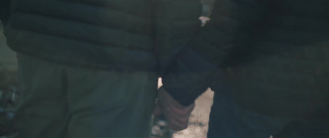 A close-up slow-motion shot of a couple holding hands in front of a sunlit frozen river on a cold winter day