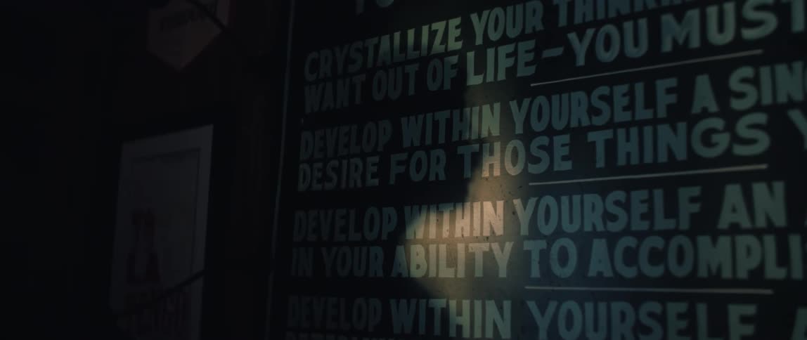 A shadow moves across an inspirational poster hanging on a wall in a dimly lit room