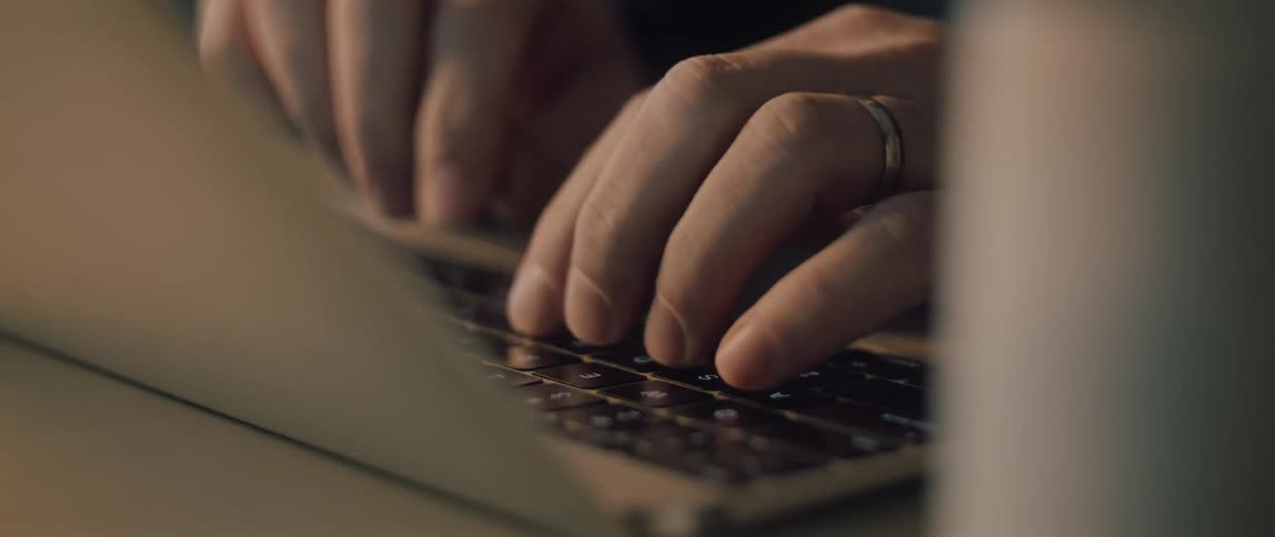 Close-up of a married person's hands quickly typing on a modern laptop keyboard in a dimly lit environment