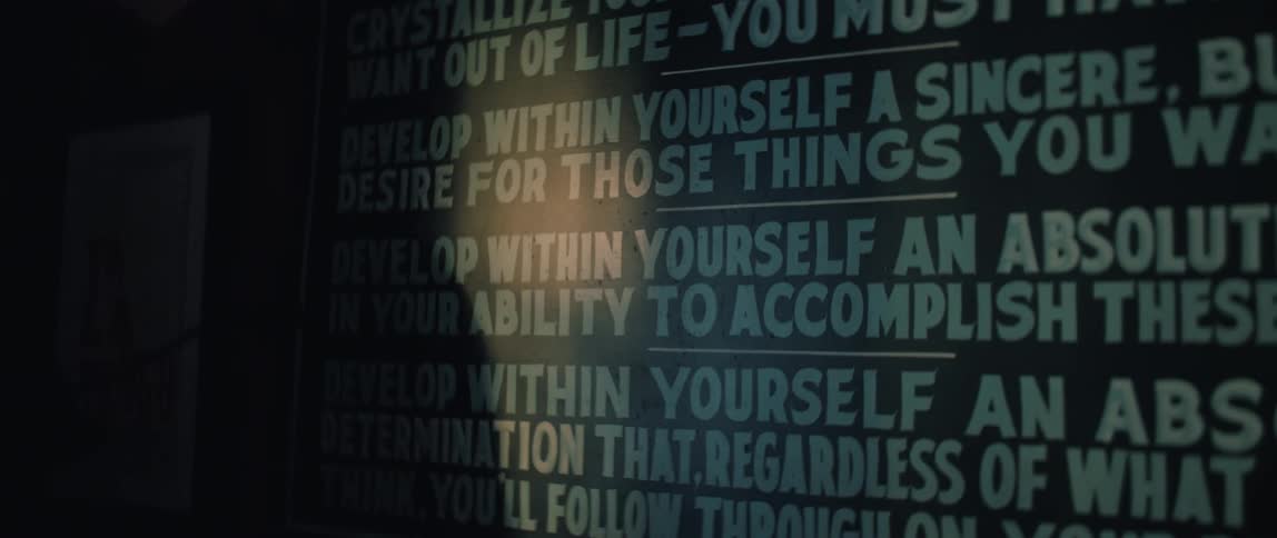 A spotlight illuminates a motivational creed on a wall as a mysterious shadow passes in front