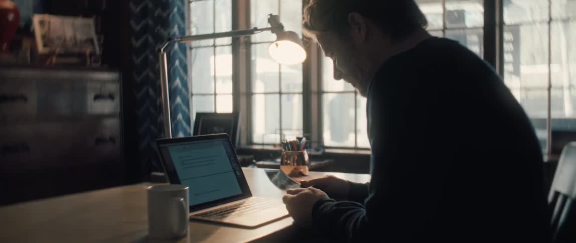 A thoughtful man working at his desk picks up an ultrasound photo and smiles at the image of his unborn child