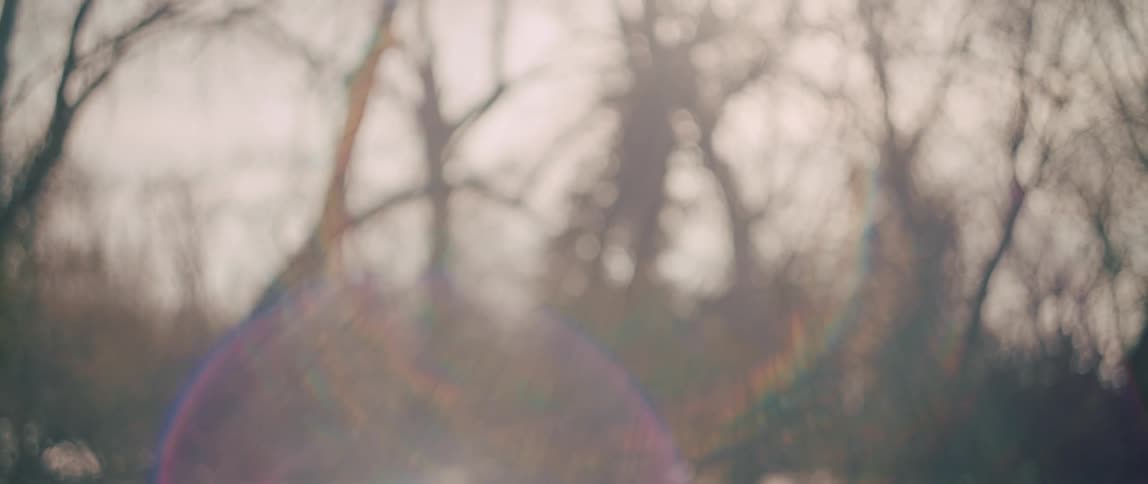 A slow-motion side view reveals a person walking through a sun-flared winter forest, creating a dreamy and contemplative atmosphere