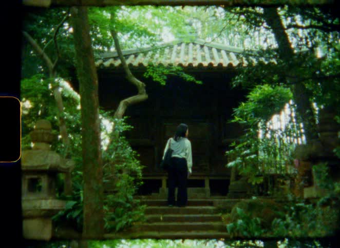A woman slowly ascends the stone steps to a secluded Japanese shrine in a lush garden, shot on vintage film