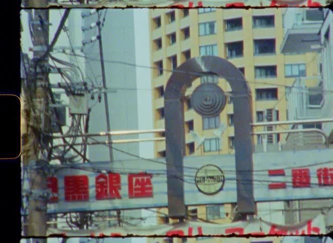 A vintage 8mm film captures the cluttered overhead power lines and street signs of Meguro Ginza in Tokyo, Japan