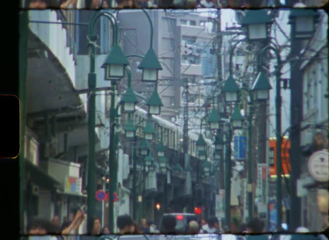 Vintage film shows a bustling street in Tokyo, Japan, as a train passes by on an elevated railway above the crowds