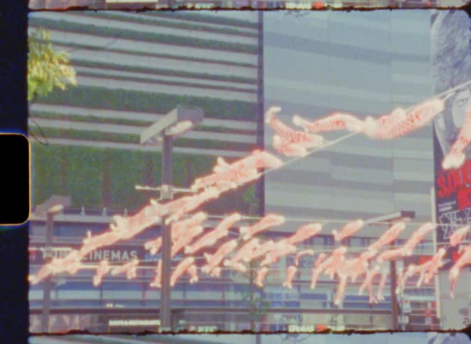 Vintage film captures koinobori carp streamers flying over a modern street in Tokyo, Japan on a sunny day