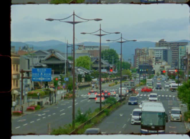High angle view on vintage film of a busy city street in Japan, where modern traffic flows alongside traditional architecture with mountains in the distance