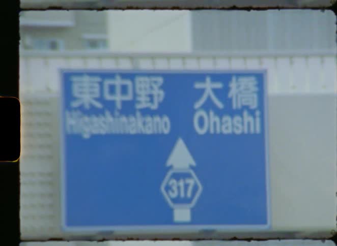 A vintage film-style shot of a blue road sign in Tokyo, Japan, giving directions to Higashinakano and Ohashi