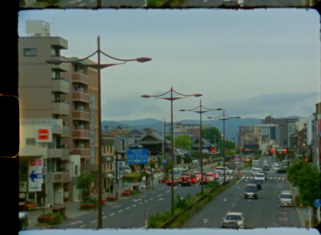 Vintage film footage captures a slow zoom-out of traffic on a busy street in Kyoto, Japan, with traditional temples and distant mountains