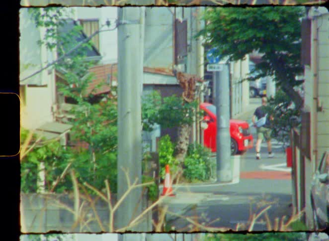 An 8mm film captures a quiet, nostalgic view of a residential street in Japan as people walk by