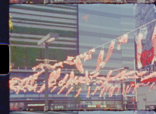 Vintage Super 8 film of traditional Japanese koinobori carp streamers gently swaying in the wind in a modern city