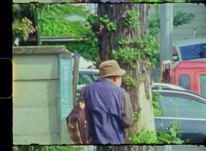 Vintage 8mm film captures the back of an elderly man with a backpack walking down a quiet street in Japan