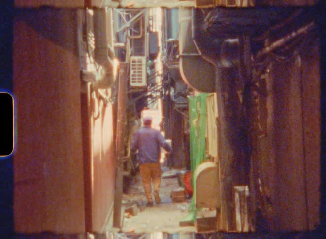 Back view of a man carrying a box as he walks away down a narrow urban alley in this Super 8mm vintage film