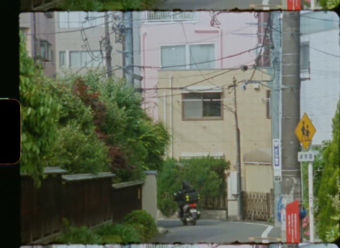 Vintage film shot of a delivery scooter driving down a quiet residential street in Tokyo, Japan