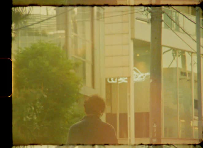 Nostalgic, dreamy 8mm film shows the silhouette of a person standing on a sunlit city street