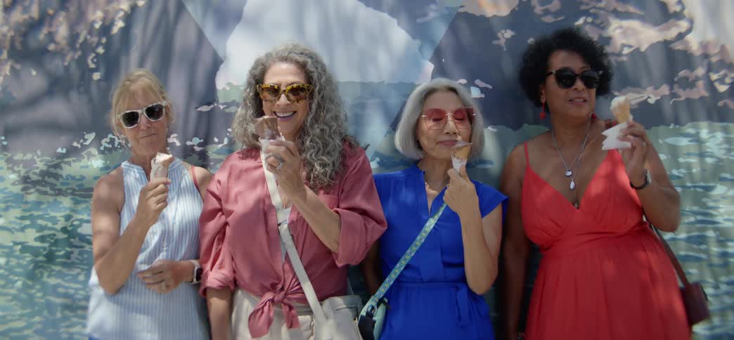 Stylish and diverse senior women friends laugh and enjoy ice cream together outdoors on a sunny day