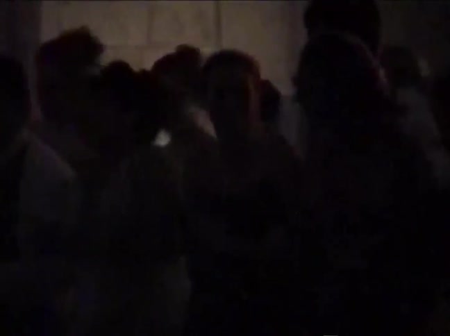 Grainy, underexposed vintage footage shows the silhouettes of people dancing at a party in a dark room