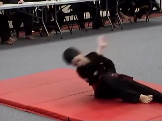 Vintage footage shows a young boy in a black uniform performing a martial arts kata on a red mat