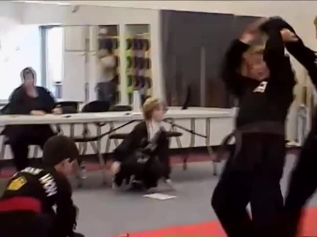 A young boy in a black uniform is thrown to the red mat by his opponent during a martial arts demonstration