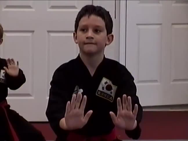 Two focused young boys in black uniforms and red belts practice synchronized martial arts forms