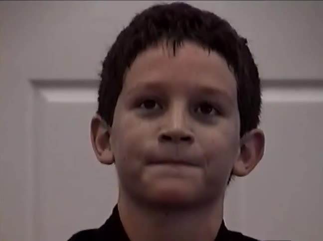 A close-up shot of a young boy in a black karate uniform smiling and focusing during his martial arts class