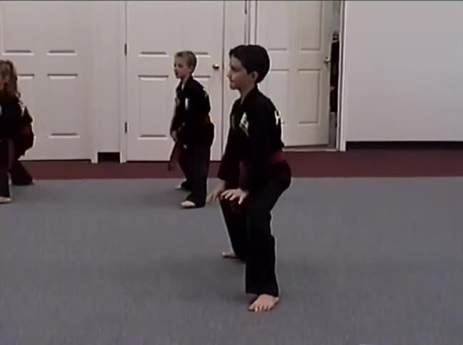 Three children in black uniforms with red belts practice a synchronized martial arts routine in a dojo