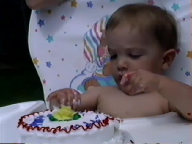 Vintage home video captures an adorable baby in a high chair making a mess while eating their first birthday cake