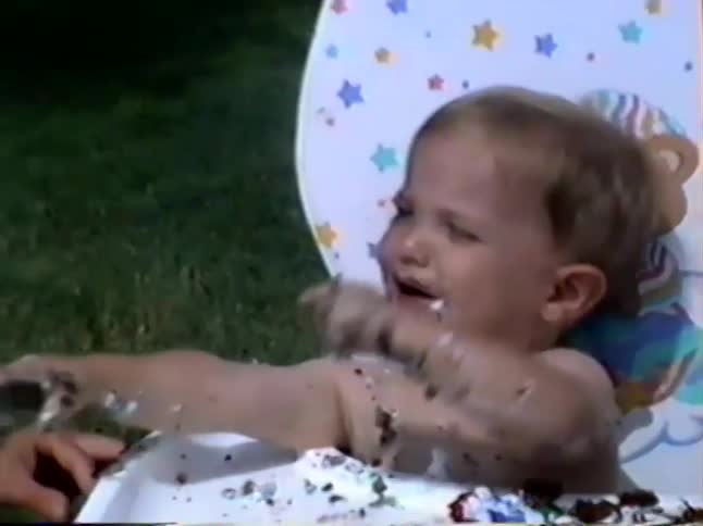 A vintage VHS clip shows a baby joyfully making a mess while eating their first birthday cake