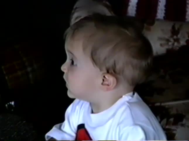 A close-up shot of a cute toddler with big eyes looking at the camera in a grainy 1990s home video