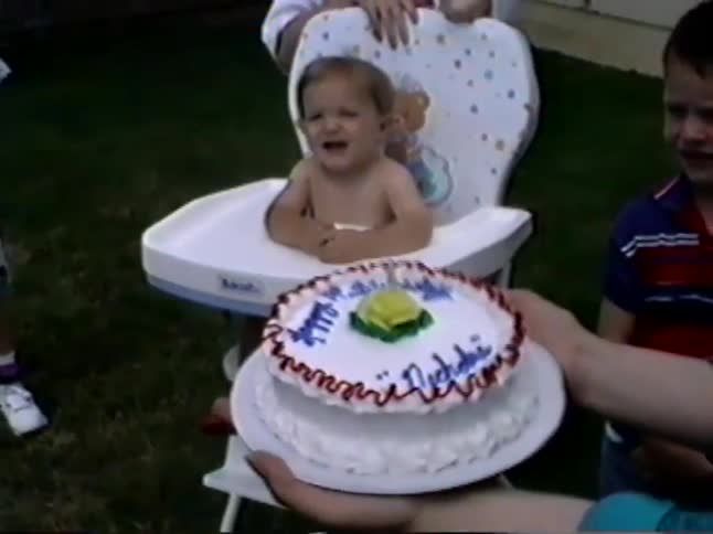 Vintage VHS footage of a baby in a high chair crying when presented with their birthday cake at a backyard party