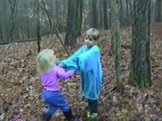 A young boy and his sister play together in the leaf-covered woods in a charming vintage home video clip