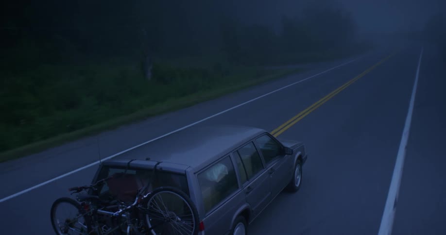 An suv carrying bicycles drives along a rural road in the mist